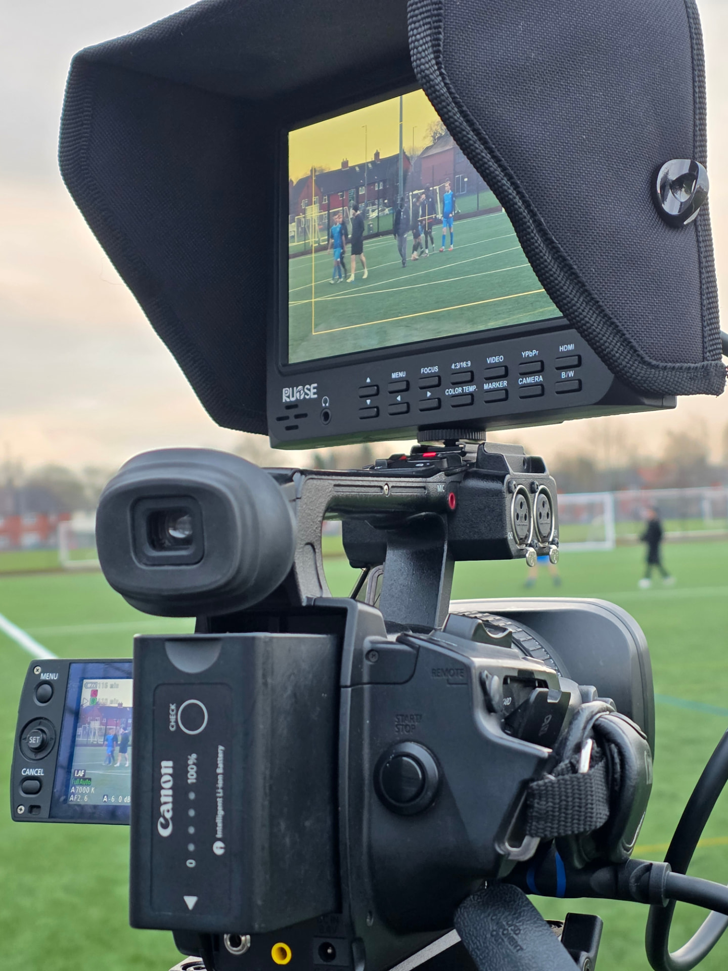 A professional camera monitor recording a football match at sunset.