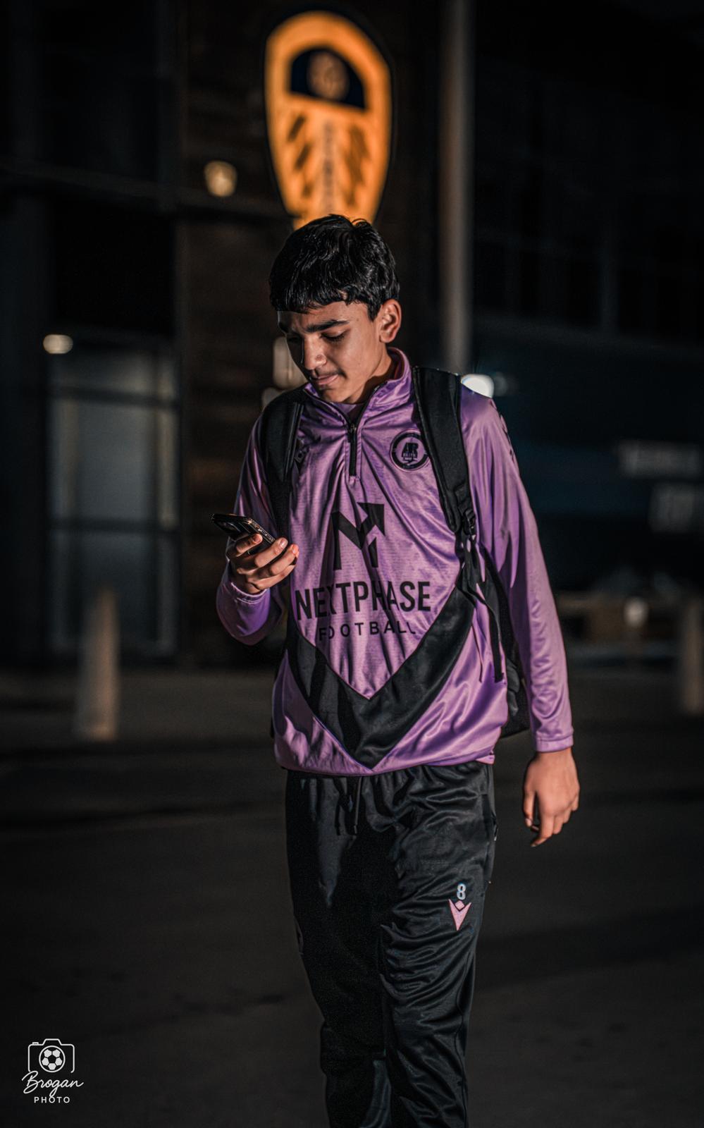 A Next Phase Football player walking outside a floodlit stadium in branded training kit.